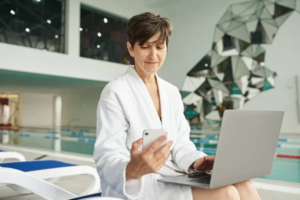 Remote work, spa center, middle aged woman using gadgets, smartphone, laptop, lounger, freelance — Stock Photo