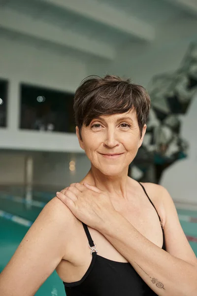 Glücklich und reif, tätowierte Frau, Sportlerin im Wellnesszentrum, Blick in die Kamera, Schwimmbad, Badebekleidung — Stockfoto
