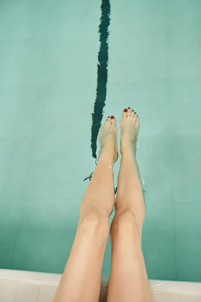 Vista superior, piernas femeninas en el agua, piscina, resort, centro de spa, interior, vista superior, vista recortada - foto de stock