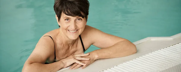 Mulher alegre e madura com tatuagem nadando na piscina, dentro de casa, centro de spa, bem-estar, bandeira — Fotografia de Stock
