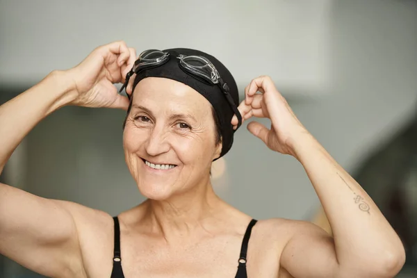 Portrait, active lifestyle, mature woman in swimwear, adjusting goggles, swim cap, spa, tattoo — Stock Photo