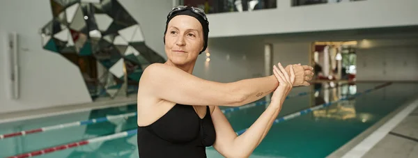 Reife Frau mit Badekappe und Schutzbrille wärmt sich in der Nähe von Schwimmbad, Wellness-Center, Badebekleidung, Banner — Stockfoto