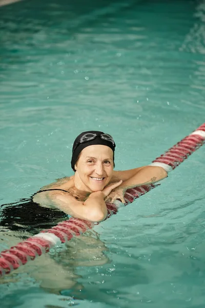 Positive Frau mittleren Alters schwimmt im Pool, Lächeln, Badekappe und -brille, gesunder Lebensstil, Sport — Stockfoto
