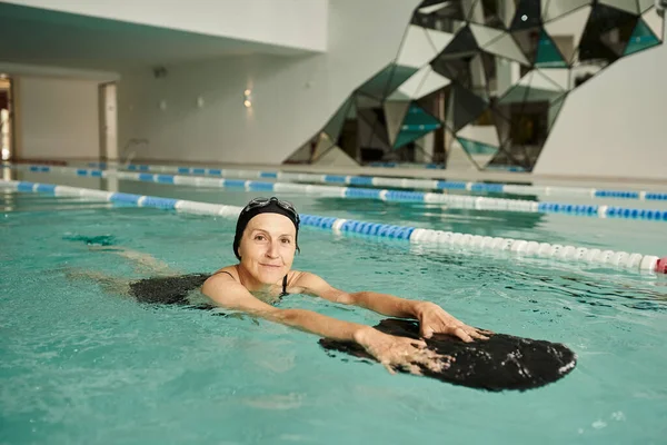 Mulher de meia idade nadando com tábua flutuante na piscina, touca de natação e óculos, esporte, estilo de vida — Fotografia de Stock