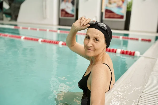 Tranquila, mujer de mediana edad que se relaja junto a la piscina, gorra de natación y gafas, deporte, centro de recreación - foto de stock