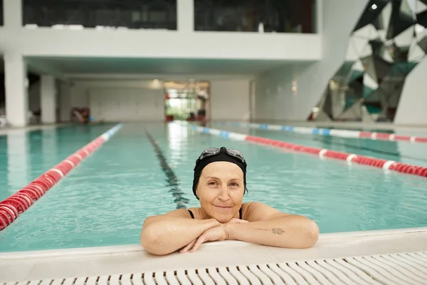 Cheerful middle aged woman relaxing at poolside, swim cap and goggles, smile, recreation center — Stock Photo