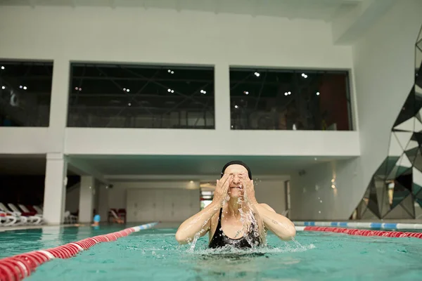 Water splashes, middle aged woman in swim cap having fun in pool, closed eyes, spa center, blissful — Stock Photo