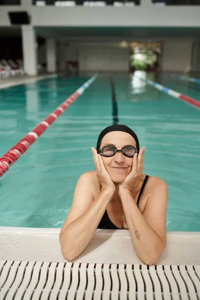 Middle aged woman in swim cap and goggles, swimming pool, recreation center, tattoo, poolside — Stock Photo