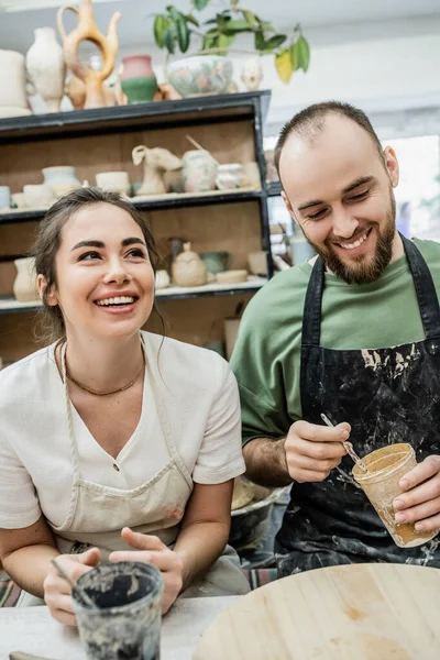 Cheerful couple of artisans holding dye while working together in ceramic workshop — Stock Photo