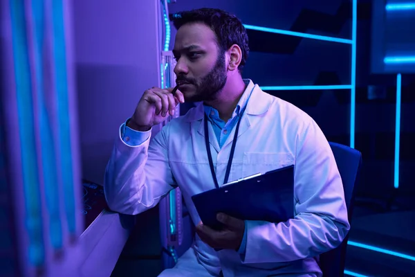 Reflexiones futuristas: Científico masculino indio contempla en medio del ambiente de neón en el centro de ciencia - foto de stock