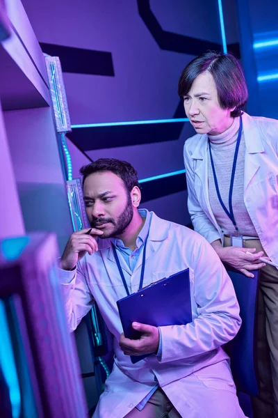 Des scientifiques hindous masculins et adultes regardent mystérieusement l'ordinateur dans le Neon-Lit Science Center — Photo de stock