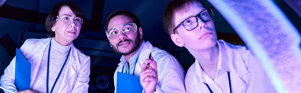 Banner, Futuristic Exploration: Diverse-Age Scientists Investigate Device in Neon-Lit Science Center — Stock Photo