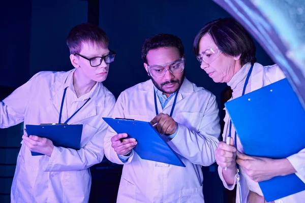 Futuristic Analysis: Scientists of Varied Ages Compare Data in Neon-Lit Science Center — Stock Photo