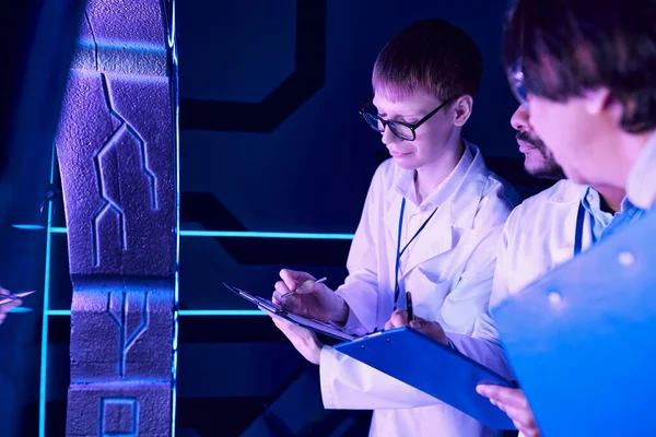 Colaboração Futurista: Cientistas em Idade Diversa trabalham perto do dispositivo no Neon-Lit Science Center — Fotografia de Stock