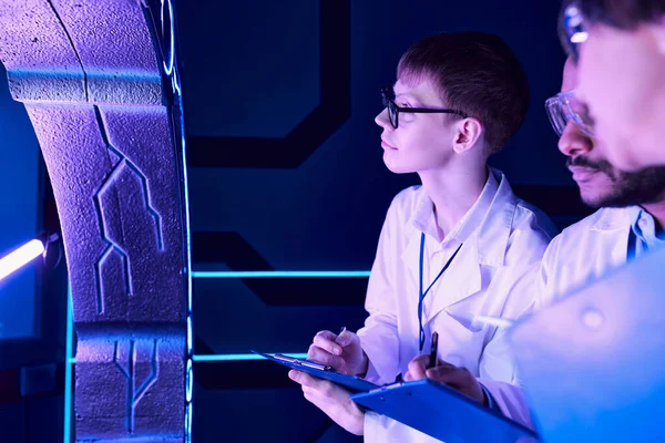 Futuristische Beobachtungen: Wissenschaftler unterschiedlichen Alters untersuchen Gerät im Neon-Lit Science Center — Stockfoto