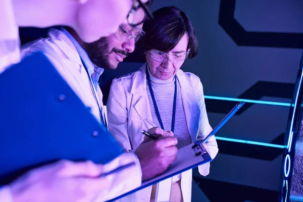 Documentación futurista: Tres científicos registran parámetros en el Neon-Lit Science Center - foto de stock