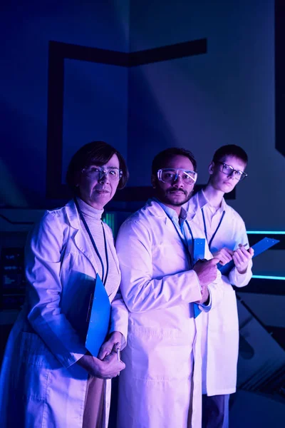 Focus futuriste : Trois scientifiques se lancent dans la tête d'affiche, regardant vers l'avenir dans le centre scientifique. — Photo de stock