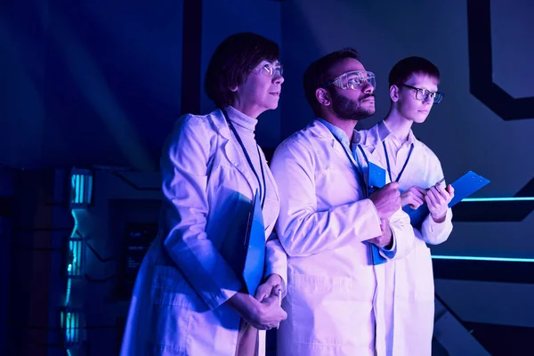 Футуристическое наблюдение: Трое ученых изучают недавно созданное устройство в научном центре неоновой литературы — стоковое фото