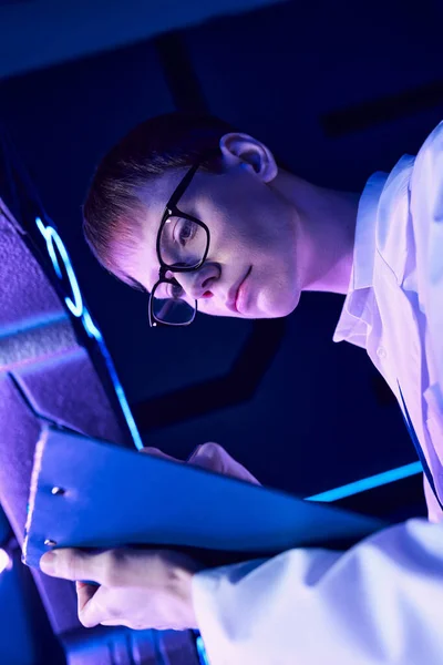 Experiencia en innovación, joven científico escribiendo en portapapeles en el centro de ciencias futuristas - foto de stock
