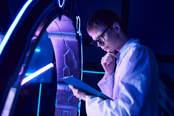 Futuristische Wissenschaft, Entdeckungszentrum, junger Wissenschaftler mit Klemmbrettdenken an innovativem Gerät — Stockfoto