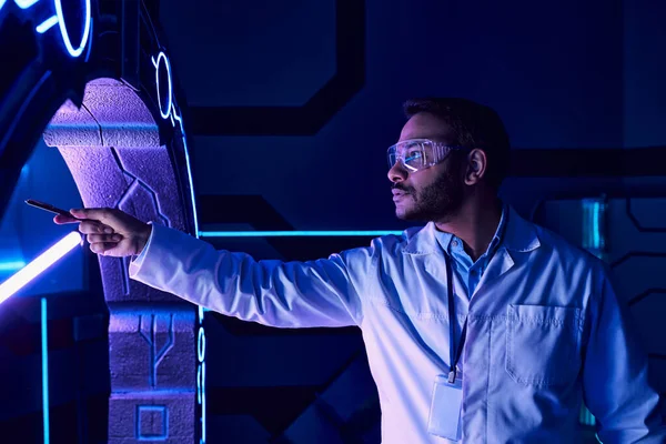 Футуристическая концепция, индийский ученый в очках, указывающий пером на новое устройство в научном центре — стоковое фото