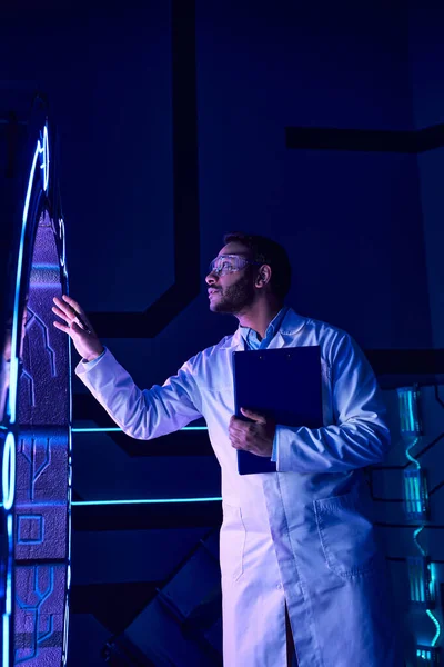 Science du futur, scientifique indien en lunettes examinant de nouveaux équipements dans le centre d'innovation néon-éclairé — Photo de stock
