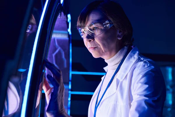 Дальновидная женщина-ученый средних лет смотрит на инновационное устройство в центре открытий — стоковое фото