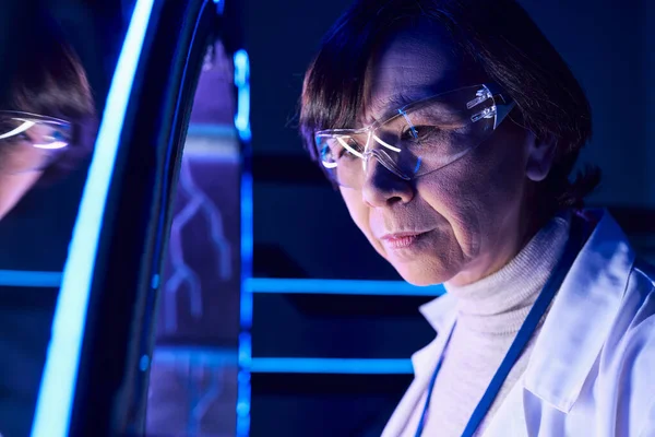Portrait of middle-aged woman scientist in goggles near new device in futuristic discovery center — Stock Photo