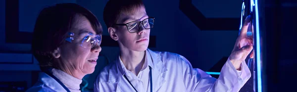 Young intern operating experimental equipment in neon-lit discovery center of future — Stock Photo