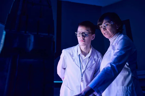 Futuristic concept, middle aged woman scientist and intern near new equipment in discovery center — Stock Photo