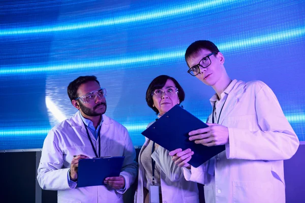 Zukunftsorientierte, junge Praktikanten, die in der Nähe multiethnischer Wissenschaftler im Innovationszentrum wegschauen — Stockfoto