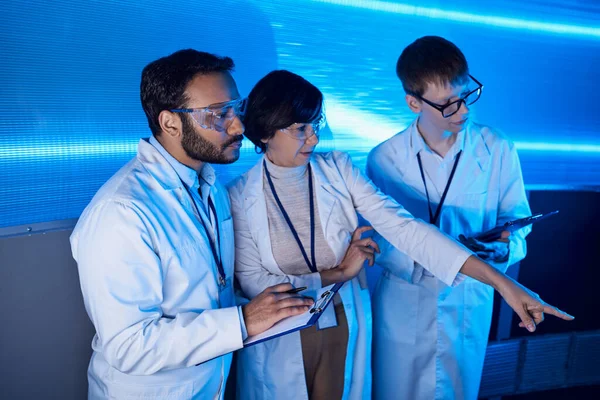 Futuristic science center, woman scientist pointing with finger near multiethnic colleagues — Stock Photo