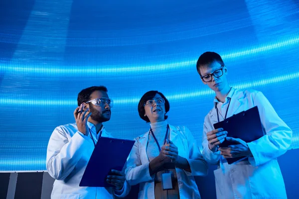 Científicos multiétnicos con portapapeles que trabajan en tecnologías futuristas en el centro científico - foto de stock