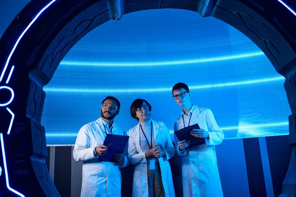 Multiethnic scientists with clipboards near experimental device in innovation hub — Stock Photo