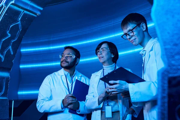 Мультиэтнические ученые, работающие на экспериментальном оборудовании рядом с улыбающимся интерном с буфером обмена — стоковое фото