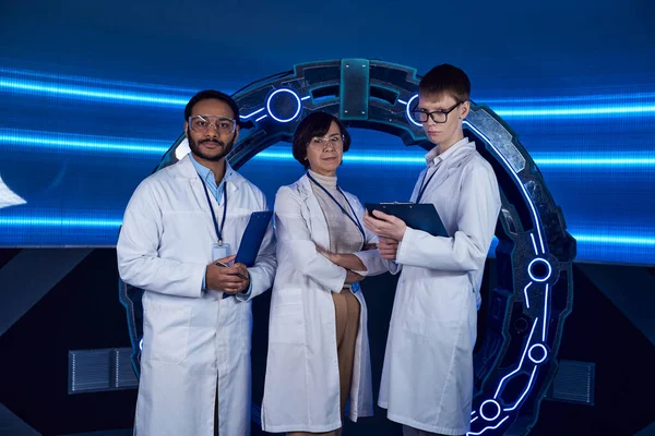 Future-oriented multiethnic scientists looking at camera near innovative device in discovery center — Stock Photo