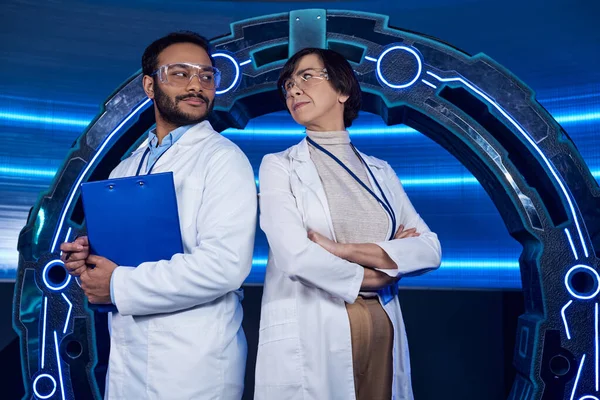 Creative multiethnic scientists looking at each other near neon-lit  device in science center — Stock Photo