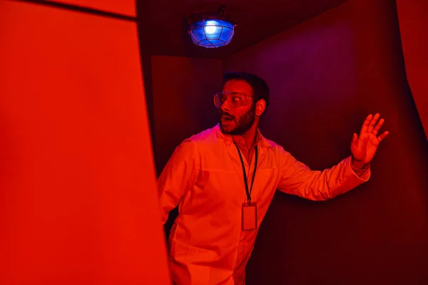 Unknown phenomenon, scared indian scientist looking away in red neon light in innovation hub — Stock Photo