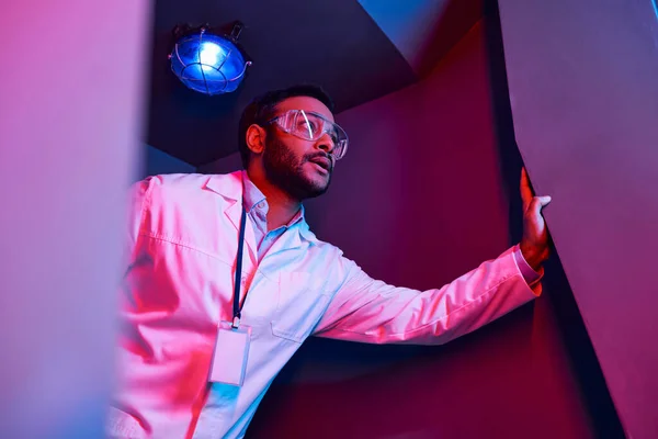 Fenômeno desconhecido, cientista indiano tenso olhando para longe no centro de ciência iluminado por néon — Fotografia de Stock