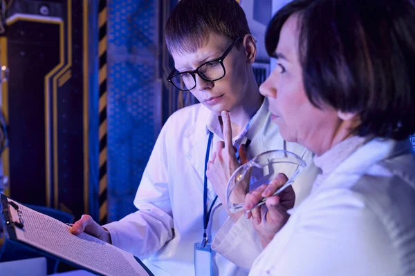 Nachdenkliche Praktikantin blickt auf Klemmbrett neben Wissenschaftlerin mit Brille im Entdeckungszentrum — Stockfoto