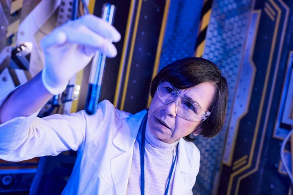 Explorando la vida de otro mundo, mujer científica sosteniendo tubo de ensayo con muestra líquida en laboratorio futurista - foto de stock