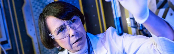 Исследование инопланетной жизни, женщина-ученый смотрит на пробирку с жидким образцом в лаборатории, баннер — стоковое фото