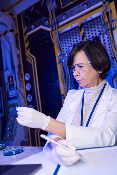 Donna scienziata in maschera guardando cartina tornasole, esplorando la vita aliena in laboratorio innovativo — Foto stock