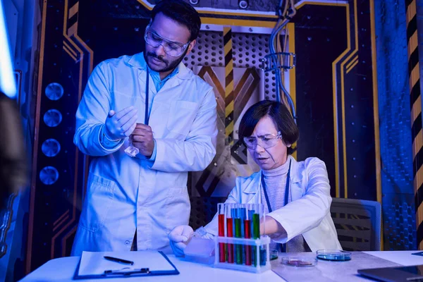 Femme scientifique travaillant avec des échantillons de vie extraterrestre près d'un collègue indien, centre de science futuriste — Photo de stock
