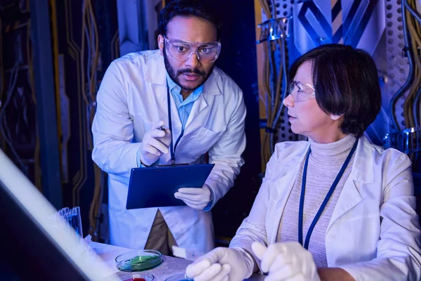 Cientista indiano apontando para amostras em vidro de laboratório perto colega explorando vida sobrenatural — Fotografia de Stock