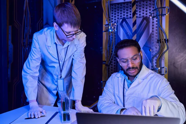 Indischer Wissenschaftler und junger Praktikant in der Nähe von Laptop und Reagenzgläsern im wissenschaftlichen Labor — Stockfoto