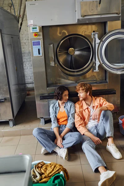 Jovem mulher asiática falando com namorado perto de roupas e máquina de lavar roupa em lavanderia pública — Fotografia de Stock