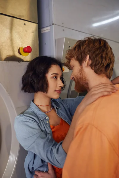 Pretty young asian woman hugging redhead boyfriend near washing machine in public laundry — Stock Photo