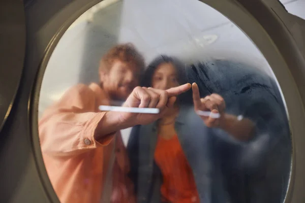 Blurred young romantic couple touching glass of washing machine in public laundry — Stock Photo