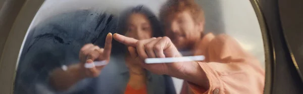 Blurred young couple touching glass of washing machine in public laundry, banner — Stock Photo